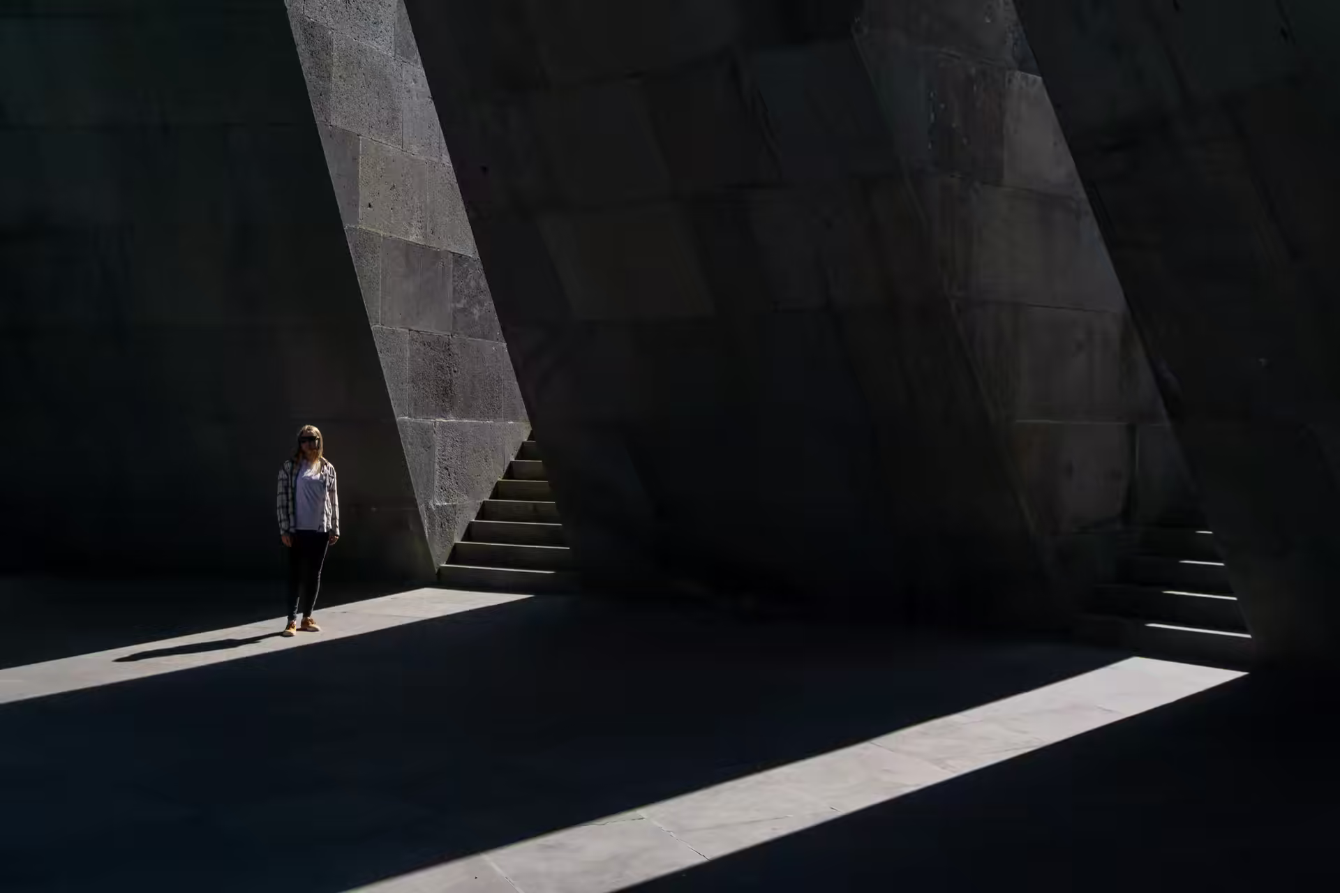 A lone figure crossing a shaft of daylight in a monumental concrete space